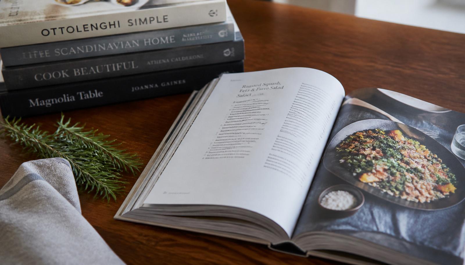 Open handwritten recipe book beside a stack of cookbooks